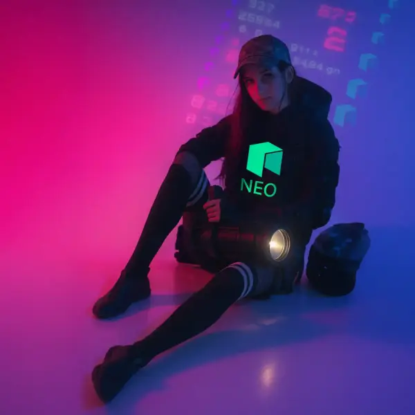 Woman in cyberpunk outfit sitting in neon-lit room, wearing a black hoodie with glowing green NEO logo – crypto streetwear aesthetic